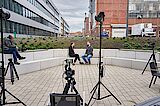 2 people surrounded by camera equipment 